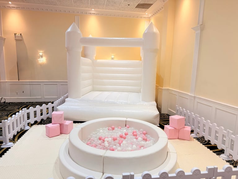 Indoor play area with white inflatable bounce house, pink and white ball pit, and pink foam blocks in an elegant white room
