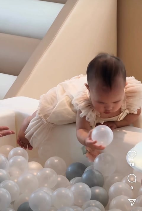 Baby in white ruffled dress playing in a ball pit with white and blue plastic balls