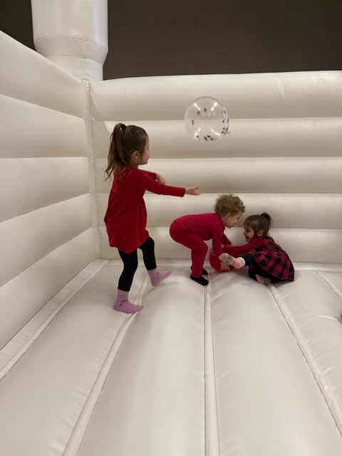 Three young children playing inside a white inflatable bounce house