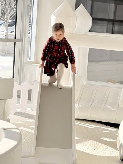 Toddler in red plaid jacket crawling through white cardboard playhouse structure indoors