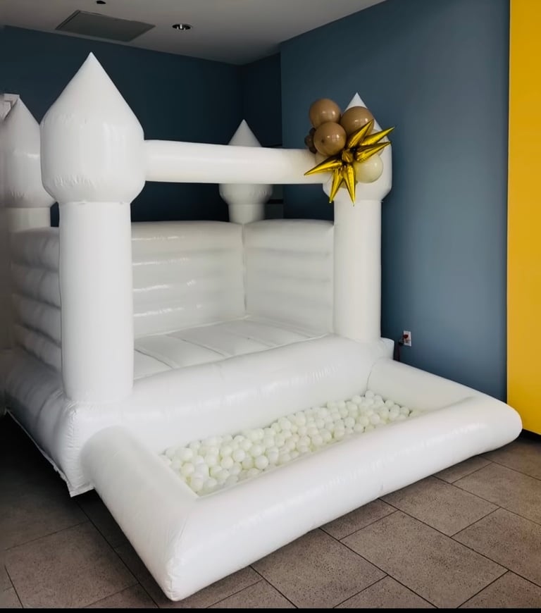 White inflatable bounce house castle with gold balloon garland in room with teal walls and yellow accent